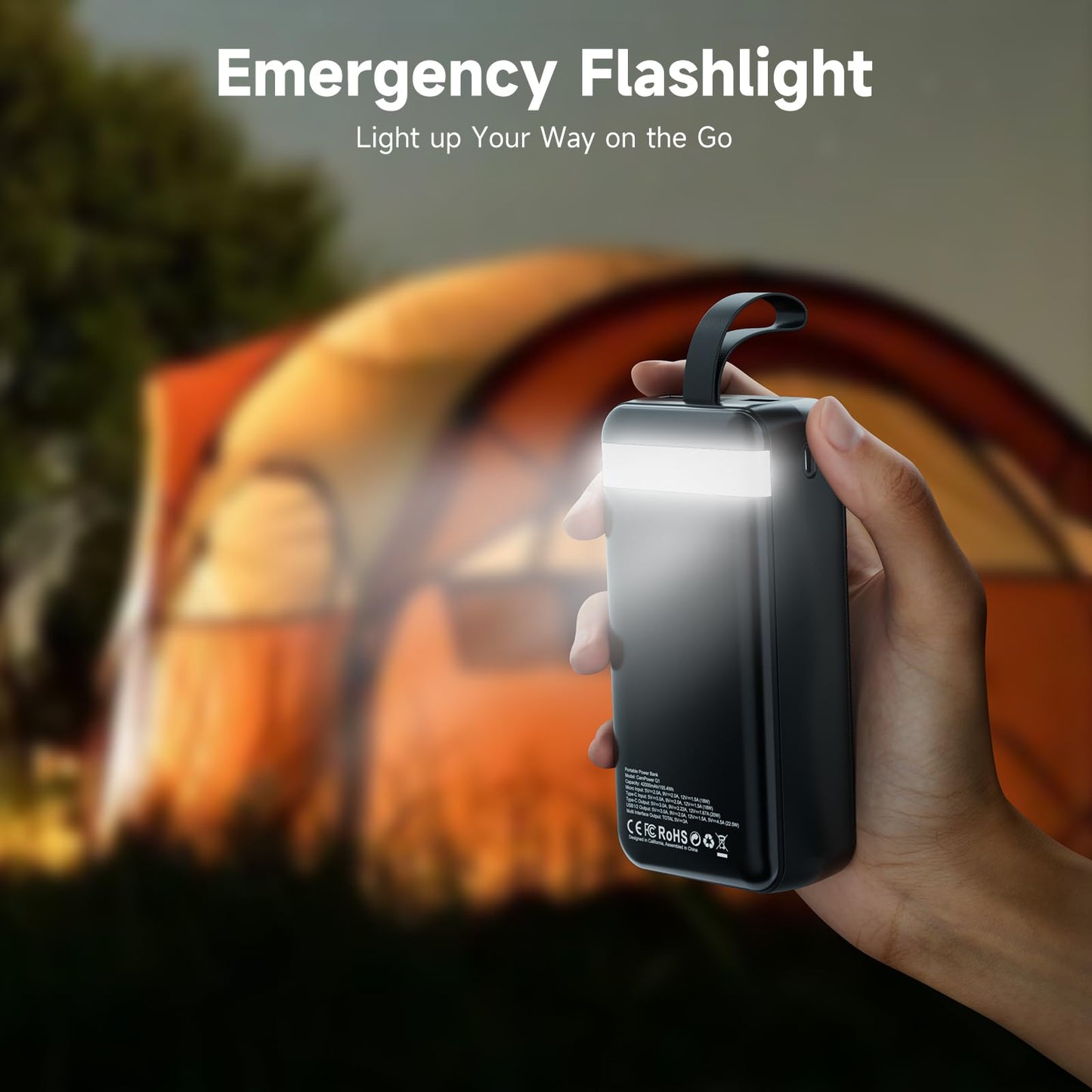 Hand holding an emergency flashlight with a blurred camping scene in the background